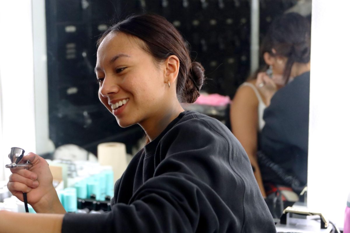 Senior May Fabriani airbrushes an ensemble member of the schoolwide musical: “The Addams Family.” This is her first year as the hair and makeup artist, having been an actor for the last three musicals. 